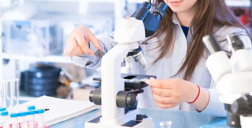 Top 10 College Courses To Take For Your Healthcare Education - Young Female Looks in Microscope | Gurnick Academy of Medical Arts
