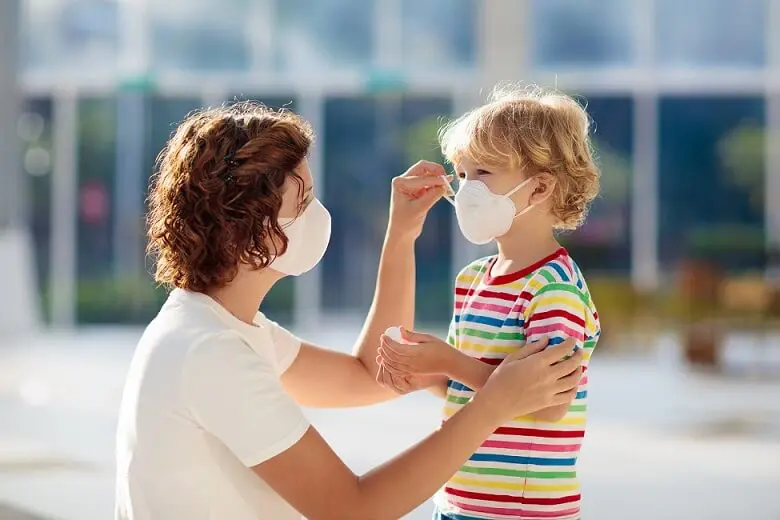 A mother wearing a facemask puts a facemask on her young daughter