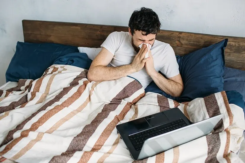 Sick young man with Novel Coronavirus 2019 (COVID-19) works from home to self-quarantine